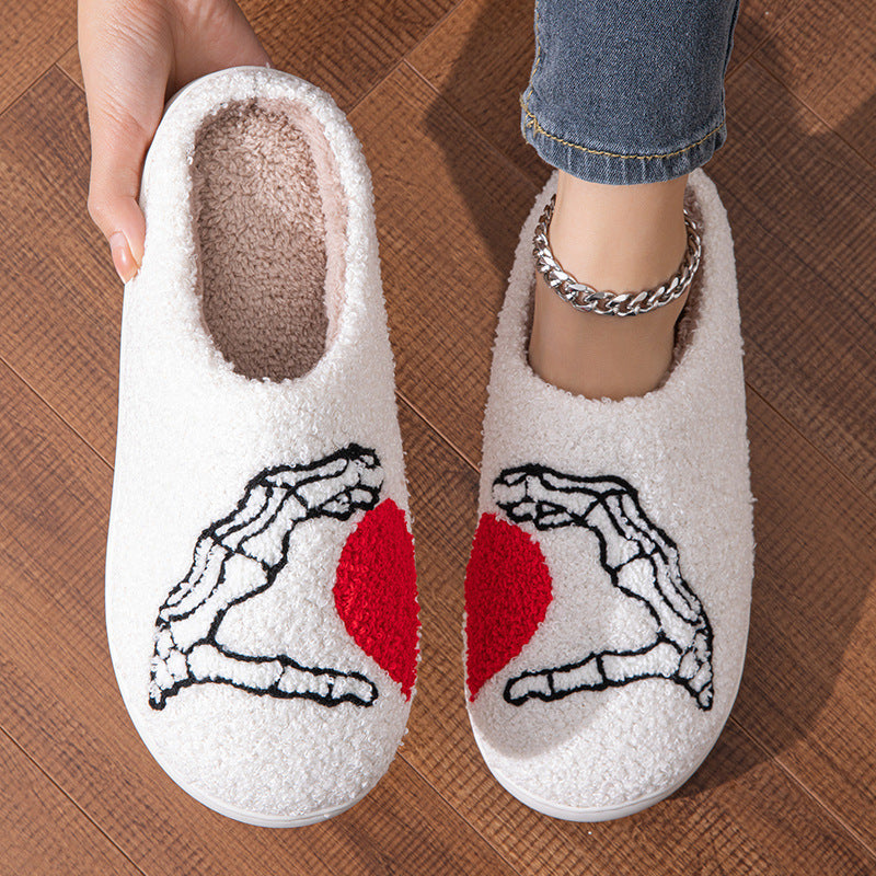 White slippers with skeleton hands and red heart design on a wooden floor.