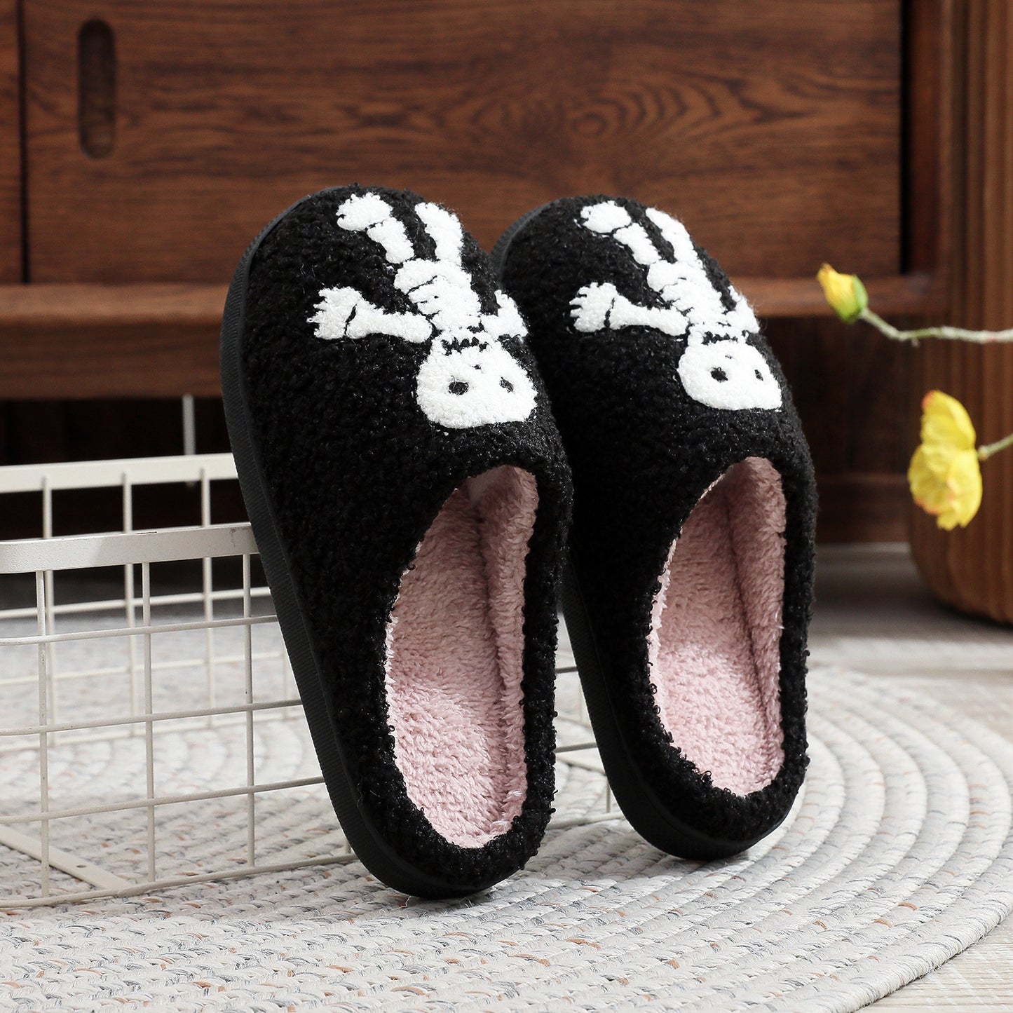 Black slippers with white skull design on a wooden floor.