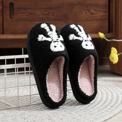 Black slippers with white skull design on a wooden floor.