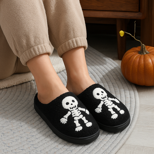 Black slippers with skeleton design worn by a person, with a pumpkin in the background.