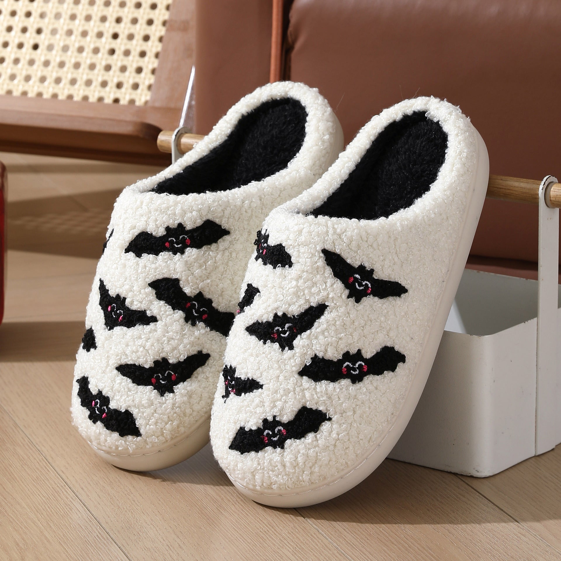 White slippers with black bat designs on a wooden floor.