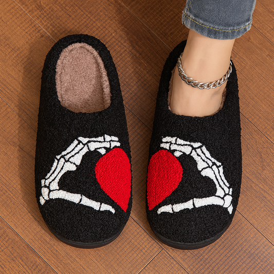 Black slippers with skeleton hands around a red heart design on a wooden floor.